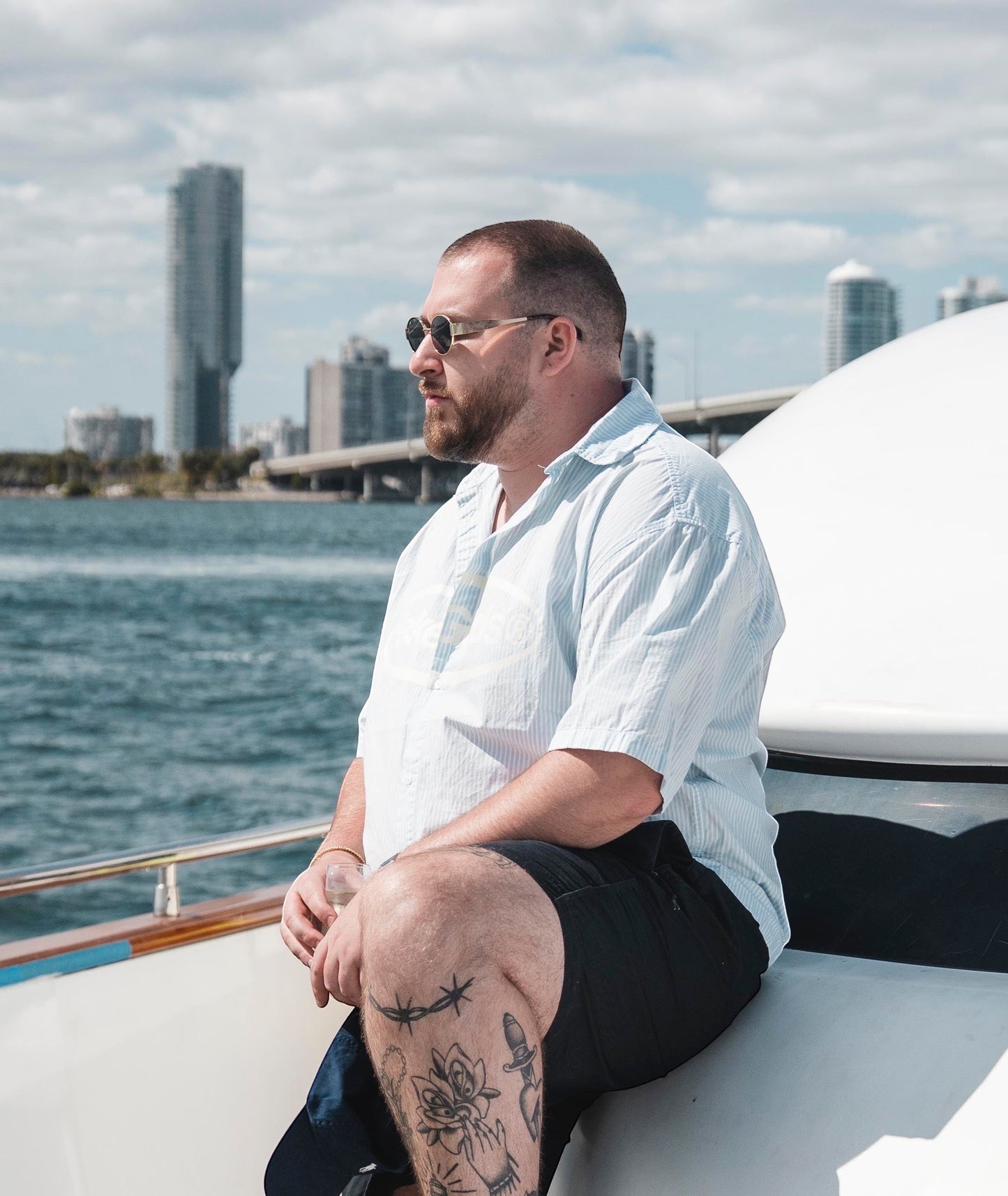 EVIE EYEWEAR MODELO IBIZA round sunglasses with gold frames on a man with tattoos sitting on a boat.