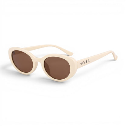Gafas de sol ovaladas TULUM de EVIE EYEWEAR en color crema con lentes marrones y detalle del logo en la patilla.